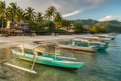 Banca boats moored off a quiet Port Barton beach with palms and village buildings behind