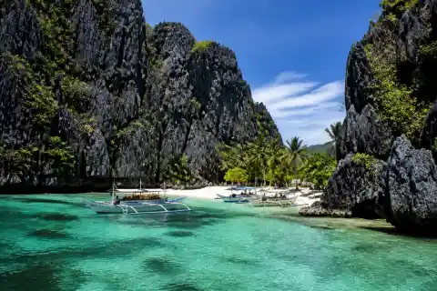 Shimizu Island beach with limestone cliffs, turquoise shallow water and small island-hopping boats