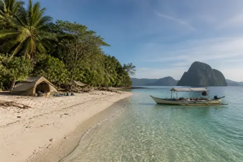 Pale-sand beach, shallow turquoise water, simple island camp and an anchored open motorboat at Sicsican Island