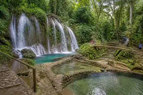 Multi‑flow Sinulom Falls with adjacent cold‑spring pools, footbridge and forested banks