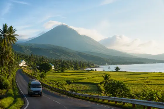 Winding provincial road with green fields and Bulusan volcano silhouette in the distance
