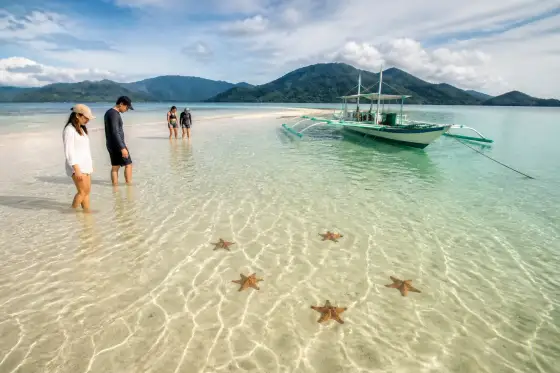 Shallow sandbar with starfish in clear water and a small outrigger boat near Port Barton