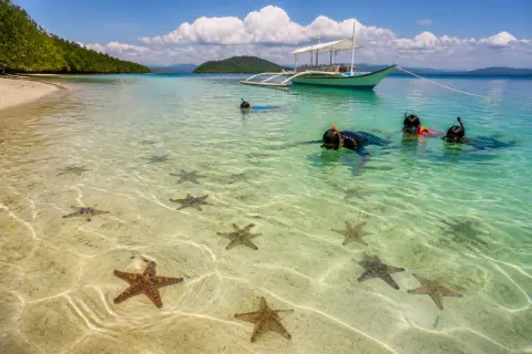 Shallow turquoise water and visible sea stars near Starfish Island with a small banca anchored offshore