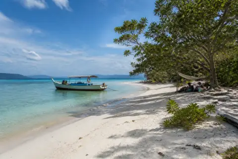 Quiet pale-sand beach on Tangkahan Island with a small expedition boat offshore