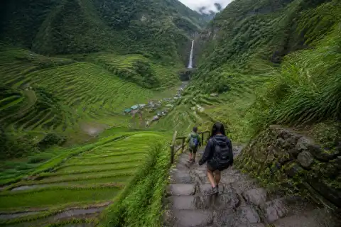 Hikers descending steep steps through Batad rice terraces toward a waterfall pool