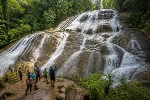 Wide multi-tiered Tarangban Falls cascading over a sloping rock face with forested surroundings and hikers at the base