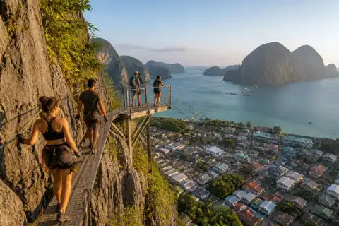 Tourists on a via‑ferrata walkway on Taraw Cliff with Bacuit Bay and limestone islands behind them