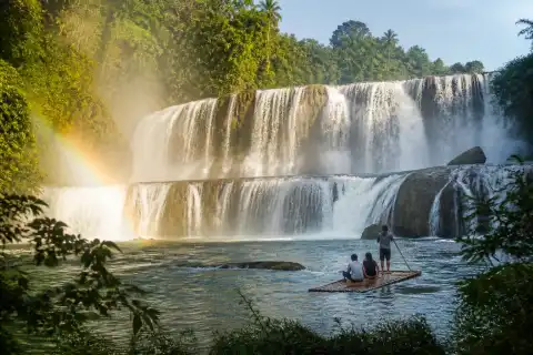 Wide curtain of Tinuy-an Falls with a bamboo raft and tropical forest backdrop