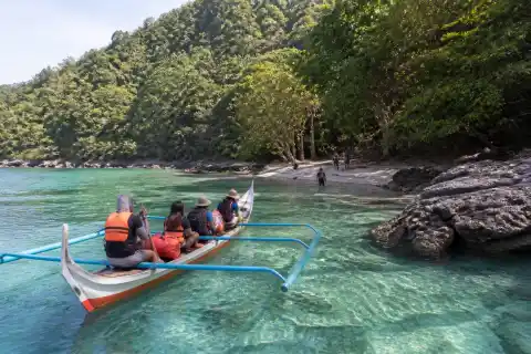 Small banca approaching a forest-backed cove at Tuka Marine Park, Kiamba
