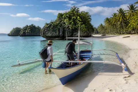 Outrigger boat on a white-sand Visayas beach with limestone islets and coconut trees