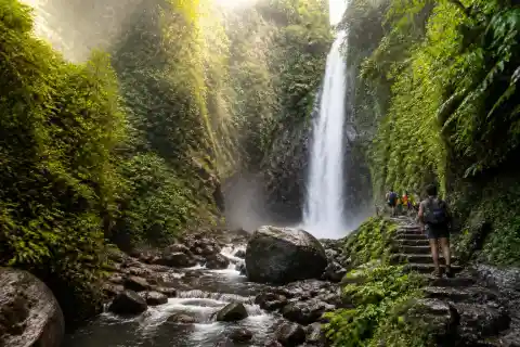 Single-drop Casaroro Falls in a boulder-filled forest gorge with mist