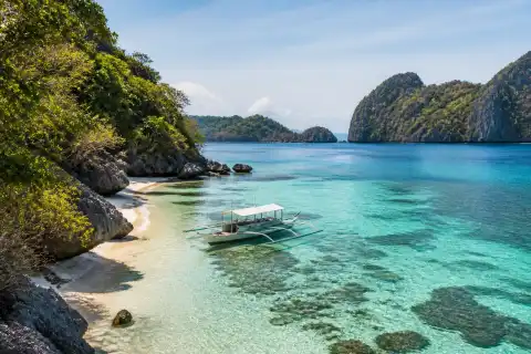Sheltered cove on Boayan Island with clear water, reef patches and a small banca anchored offshore