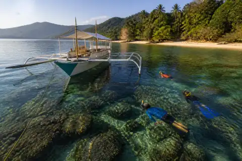 Snorkelers and a small outrigger boat over clear reef water near Port Barton, Palawan