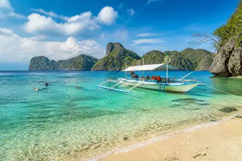 Bangka anchored off Shimizu Island with snorkelers in clear water and limestone cliffs in the background