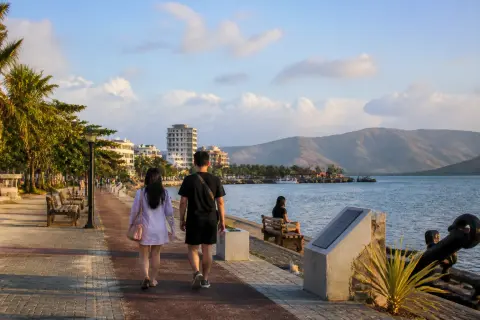 People walking along Subic Bay Boardwalk with bay and memorials at sunset