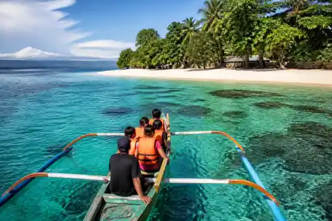 Banca approaching a white-sand beach on Talikud Island with clear turquoise water
