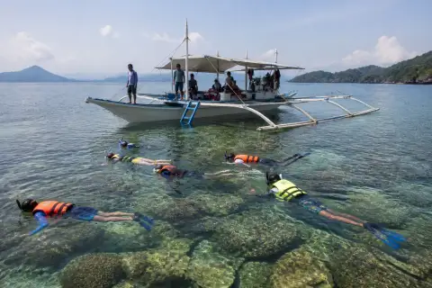 Banca and snorkelers floating over shallow coral at Twin Reef, Port Barton