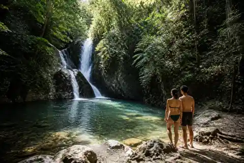 Tropical waterfall feeding a shaded natural pool with forest vegetation and visitors at the water’s edge