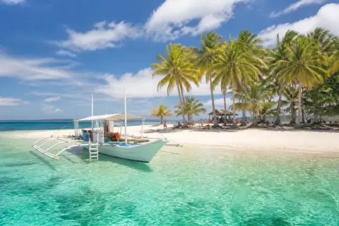 White‑sand island beach with coconut palms and an anchored banca boat in Siargao