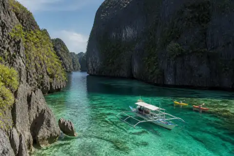 Sheltered turquoise Cadlao Lagoon framed by limestone karst cliffs with a small boat and kayaks