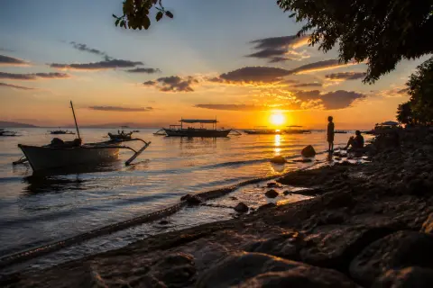 Silhouetted boats and rocky Panagsama coastline at sunset in Moalboal